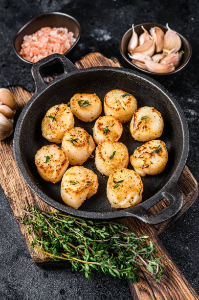 istock Fried scallops with butter sauce in a pan. Black background. Top view 1332072334