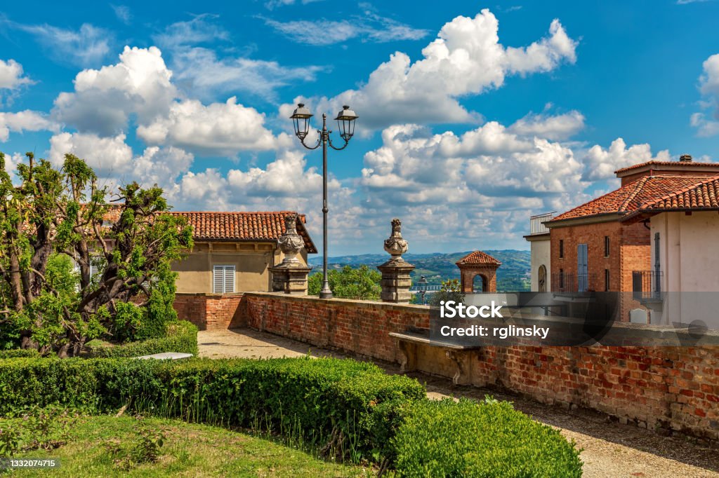 Small park and houses under beautiful sky in Govone, Italy. Green bushes in the park and typical houses under beautiful blue sky with white clouds in small town of Govone in Piedmont, Northern Italy. Architecture Stock Photo