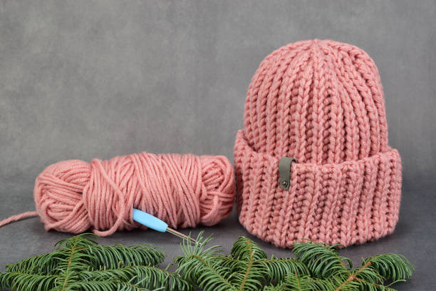 두꺼운 분홍색 원사에서 니트 겨울 모자. 근처에는 크로 셰 뜨개질 후크가 붙어있는 원사의 유적이 있습니다. - crochet knitting hat wool 뉴스 사진 이미지