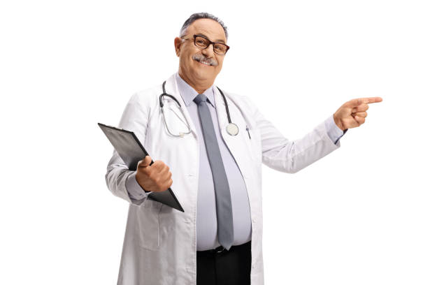 istock Smiling mature doctor standing with a clipboard and pointing 1332077992