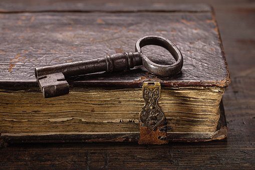 On an old book with clasps, there is an old key made of metal. Antique objects on a dark wooden background.