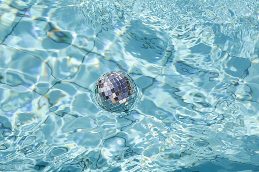 silver disco ball floating in blue water in pool. Christmas and happy new year concept.