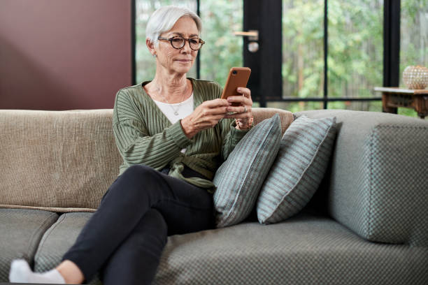 istock Shot of a senior woman using a cellphone while relaxing on a sofa at home 1332083599