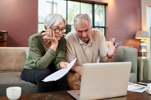 shot of a senior couple using a laptop while going through paperwork at home - inheritance tax imagens e fotografias de stock