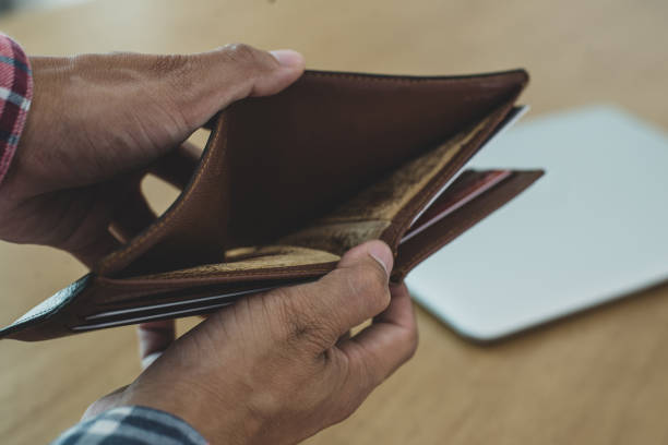 istock Young man hands holding brown opened empty wallet on wooden table with laptop background. He was in financial trouble after being laid off due to the coronavirus pandemic. 1332087253