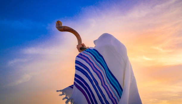 Blowing traditional ram's horn, Shofar Blowing the shofar for the Feast of Trumpets - Jewish man in a traditional tallit prayer shawl blowing the ram's horn against beautiful sunset sky orthodox judaism photos stock pictures, royalty-free photos & images