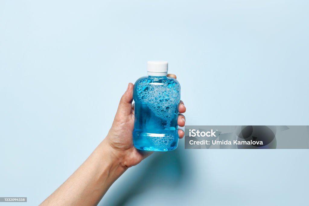 Hand holds mouth refreshing liquid Hand holds a bottle of breath freshener. A person hand holding a mouth refreshing liquid on bright blue background Mouthwash Stock Photo