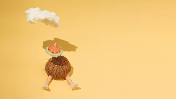 istock Half a coconut, an umbrella and the doll's legs protrude from it, a cloud casts a shadow on a yellow background, summer 1332097290