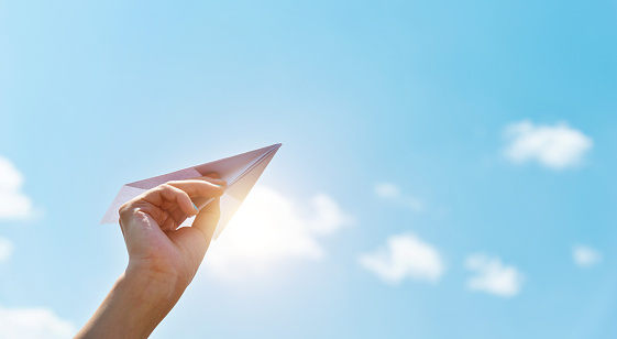 Woman hand holding a paper plane under blue sky.