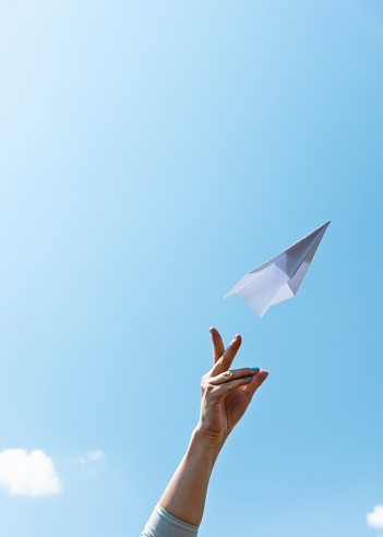 Woman hand throwing paper airplane on blue sky.