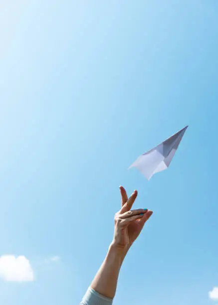 Photo of Woman hand throwing paper airplane on blue sky