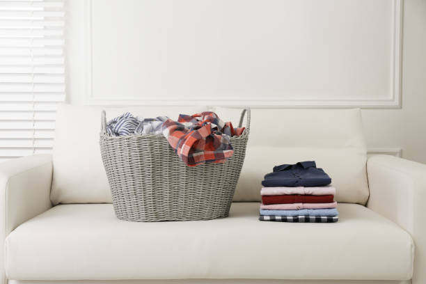 istock Wicker basket with dirty laundry and stack of clean clothes on sofa indoors 1332097520