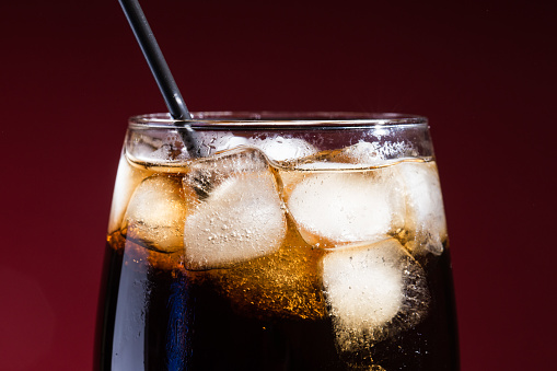 A glass of cola beverage with a salt. On a red background.