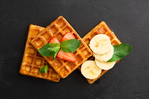 Belgium waffles with strawberry, banana and mint on black stone background. Closeup view. Breakfast concept. Top view. FLat lay