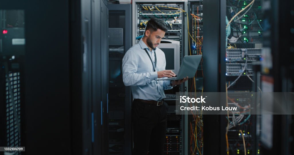 Shot of a young male engineer using his laptop in a server room Finding the source of the problem Technology Stock Photo