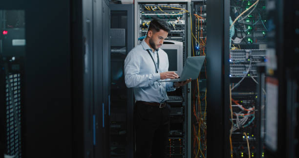 tiro de um jovem engenheiro usando seu laptop em uma sala de servidor - network server technology computer computer network - fotografias e filmes do acervo