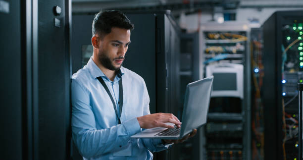 istock Shot of a young male engineer using his laptop in a server room 1332104712