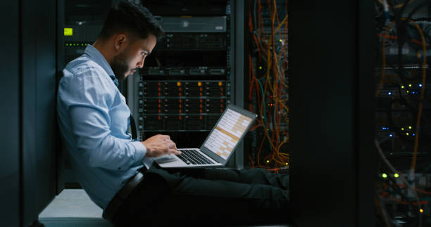 istock Shot of a young male engineer using his laptop in a server room 1332104725
