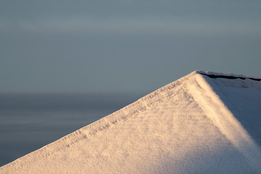 Rooftop covered with fresh snow in golden light (golden hour) on an early winter morning just after sunrise.