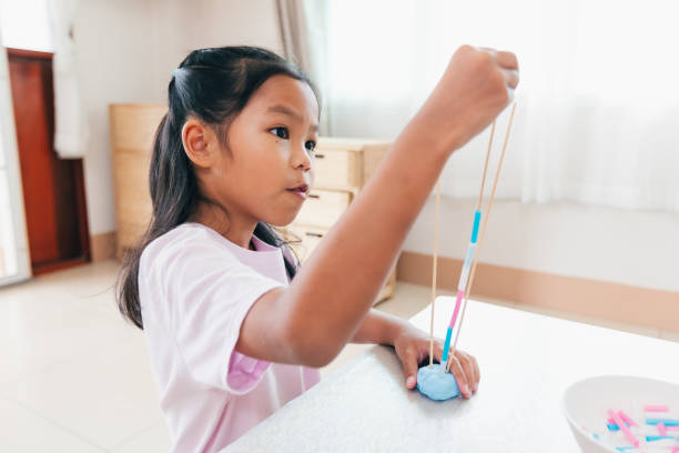 menina asiática bonita brincando e criando com playdough e canudos. criança concentrada com playdough construindo um modelo de molécula. - skill child mathematics physics - fotografias e filmes do acervo