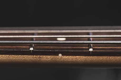 A detail shot of a neck of a western guitarin front of a grey background.
