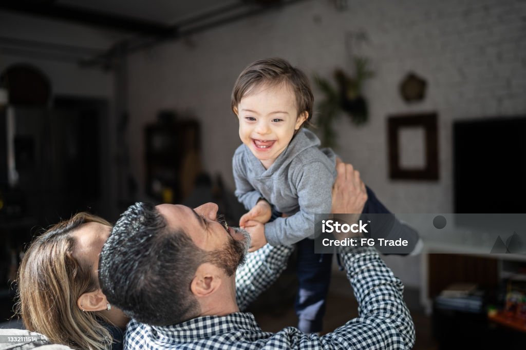 Mature couple playing with son with special needs at home Down Syndrome Stock Photo