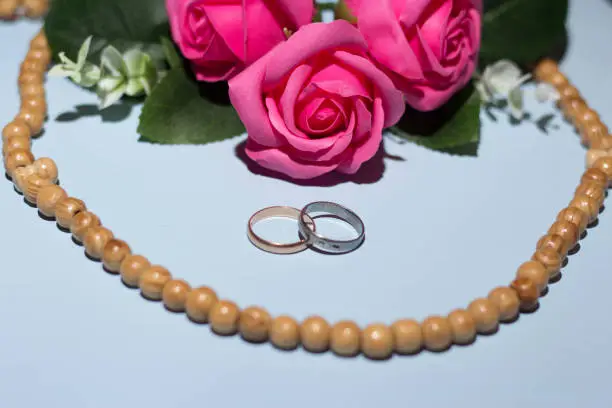 Gold and silver wedding ring, pink roses, tasbeeh rosary beads. Islamic wedding concept.