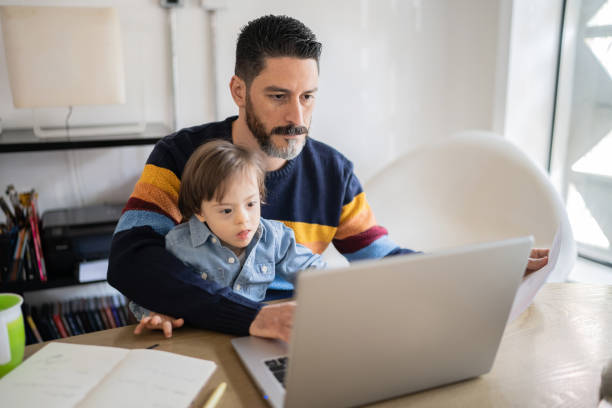 istock Mature man working at home with baby son - boy with special needs 1332112125