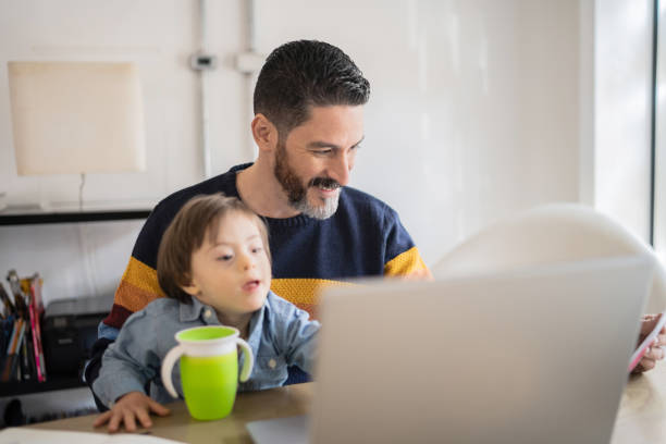 istock Mature man working at home with baby son - boy with special needs 1332112128