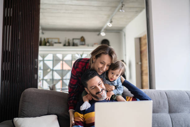 homme utilisant un ordinateur portable et étant embrassé par sa femme et son fils ayant des besoins spéciaux à la maison - caucasian male female offspring photos et images de collection