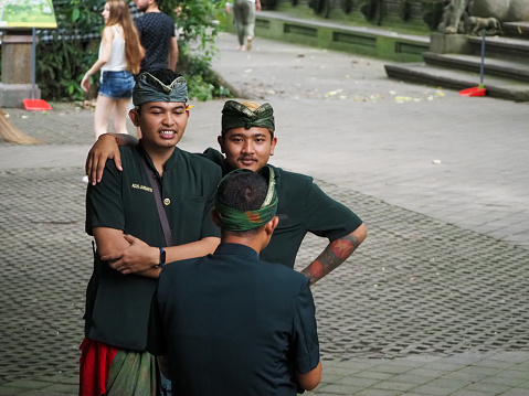 Closeup photo of male Balinese grounds personnel in the Sacred Ubud Monkey Forest. The men are dressed in an official green uniform of a traditional sarong, jacket and bandana. Their job is to supervise tourists and feed the Macaque monkeys.