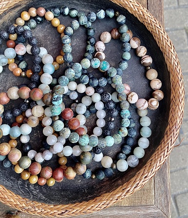Vertical close up of art in the everyday: earth color crystal bracelets in wicker and stone basket at artisan markets Byron Bay