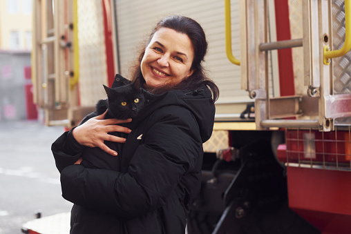 Mujer feliz sostiene su gato negro en las manos ner camión de bomberos al aire libre photo