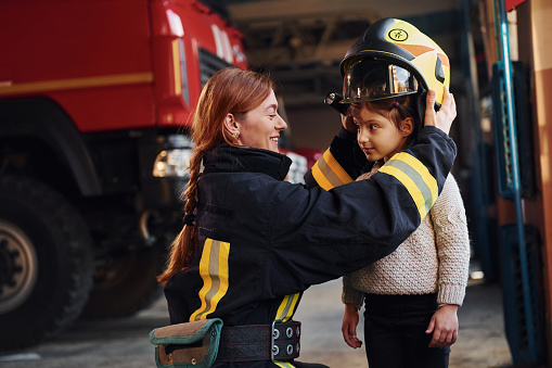 Niña feliz está con la mujer bombero en uniforme de protección photo