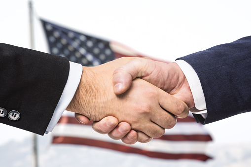 Two businessmen shake hands on the background of USA flag, partnership concept, close up
