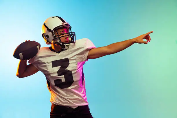 Fast serve. Portrait of male american football player playing, training isolated on blue background in neon light. Concept of sport, movement, achievements. Copy space for ad