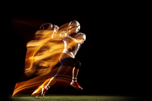 Unstoppable. Portrait of young man, American football player training isolated on dark studio background with mixed neon light. Concept of sport, movement, achievements. Copy space for ad
