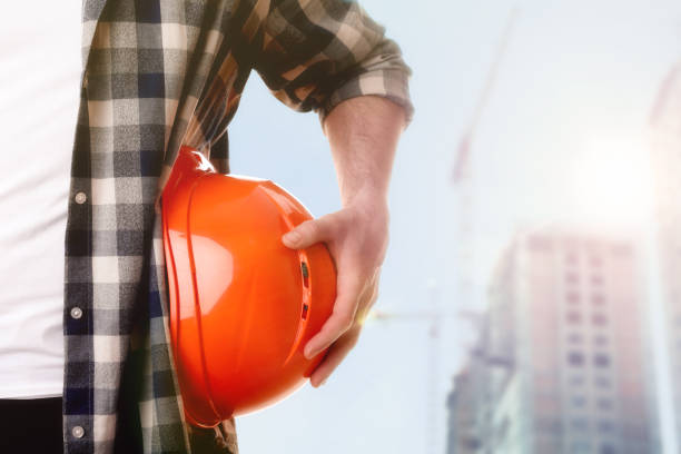 istock Man with orange hard hat at construction site with unfinished building, closeup. Space for text 1332130707