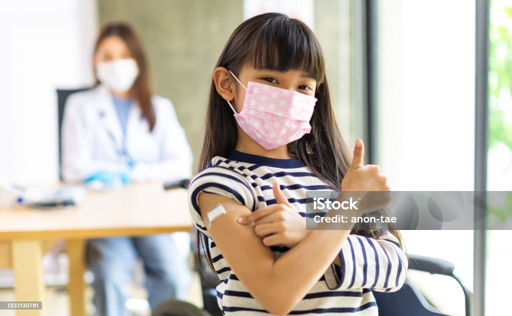 Asian doctor wearing gloves and isolation mask is making a COVID-19 vaccination in the shoulder of child patienr at hospital. Asian  doctor wearing gloves and isolation mask is making a COVID-19 vaccination in the shoulder of child patient  at hospital. Child Stock Photo