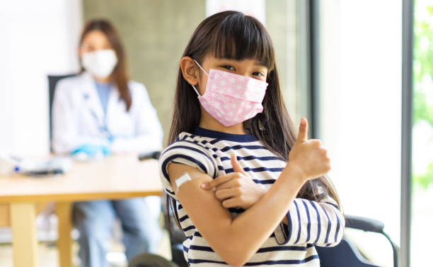 médico asiático usando luvas e máscara de isolamento está fazendo uma vacinação covid-19 no ombro de criança patienr no hospital. - vacina - fotografias e filmes do acervo