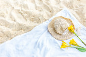 straw hat and yellow flower on white beach towel on a sandy background, top view