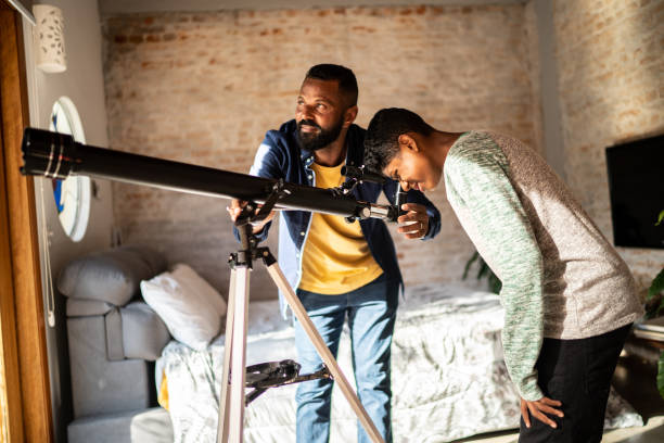 padre e hijo con telescopio mirando al cielo desde casa - curiosity searching discovery home interior fotografías e imágenes de stock