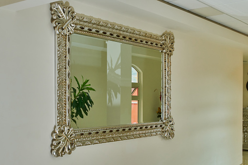 Large mirror with a luxurious colonial Victorian style frame hung on a white wall in a hallway