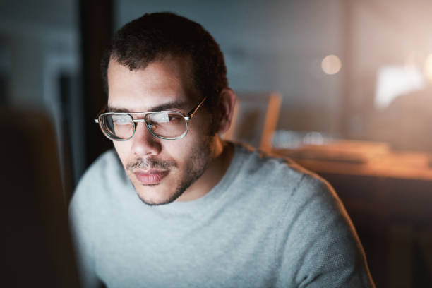 istock Closeup shot of a young man using his computer late at night at the office 1332137802