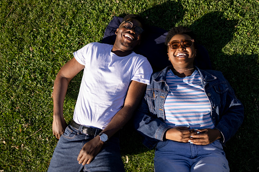 View from directly above of a young happy African American couple having fun together in nature, lying down on the grass and enjoying themselves, smiling