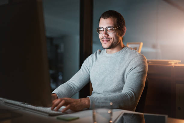 istock Shot of a young man looking pleased while using the computer at night at the office 1332137874