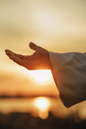 Jesus Christ reaching out his hand for help against background of sunset sky. Closeup.