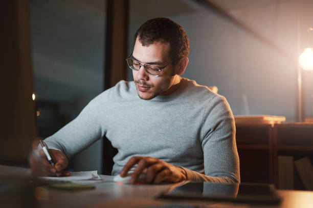 istock Shot of a young man making notes while working late at night on the computer at work 1332138742