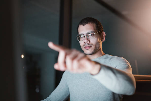 Shot of a man pointing to his monitor while using his computer at night at work