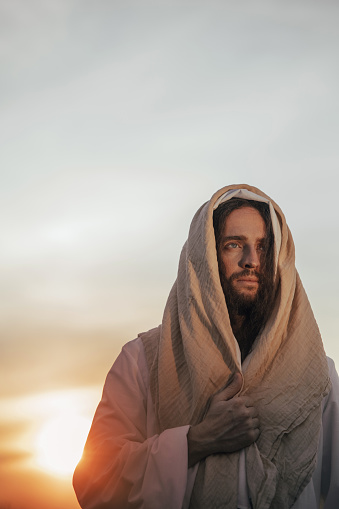 Portrait of Jesus Christ in his traditional white robe against sunset sky background.